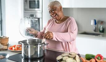 feliz Senior mulher tendo Diversão preparando almoço dentro moderno cozinha - hispânico mãe cozinhando para a família às casa foto