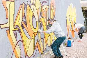 grafite artistas pintura colorida mural em uma cinzento parede - criativo homens realizando desenhando murais - conceito do rua e moderno arte, cultura e juventude estilo de vida foto