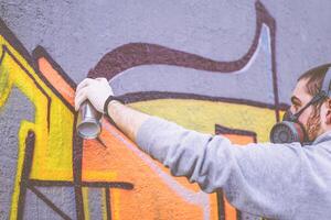 rua artista pintura com uma cor spray pode uma grafite em uma parede ao ar livre - urbano homem realizando com murales - conceito do moderno contemporâneo arte - foco em dele mão foto