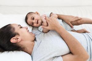 feliz mãe deitado em cama com dela pequeno bebê - família e maternidade conceito foto