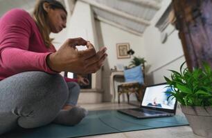 latim maduro mulher fazendo ioga virtual ginástica classe com computador portátil às casa - e-learning e pessoas bem estar estilo de vida conceito foto