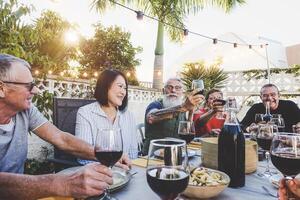 feliz família comendo e bebendo vermelho vinho às jantar churrasco festa ao ar livre - aposentado amigos tendo Diversão jantar juntos às restaurante - conceito do Comida e beber com idosos final de semana estilo de vida pessoas foto