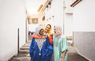 feliz muçulmano mulheres caminhando dentro a cidade Centro - árabe jovem meninas tendo Diversão gastos Tempo e rindo juntos ao ar livre - conceito do estilo de vida pessoas cultura e religião foto