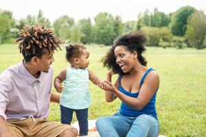 feliz africano família tendo Diversão dentro público parque - mãe e pai com seus filha desfrutando Tempo juntos durante final de semana ao ar livre - pais amor e mãe dia conceito foto