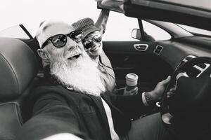 feliz Senior casal levando selfie em Novo conversível carro - maduro pessoas tendo Diversão juntos durante estrada viagem período de férias - idosos estilo de vida e viagem transporte conceito - Preto e branco edição foto