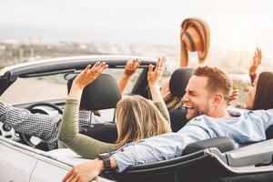 grupo do amigos tendo Diversão dentro conversível carro durante estrada viagem às pôr do sol - jovem viagem pessoas dirigindo uma cabriolet durante verão feriados - felicidade, período de férias e juventude estilo de vida conceito foto