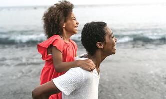 feliz afro mãe e filha tendo Diversão em a de praia durante Férias - adorável família estilo de vida conceito foto