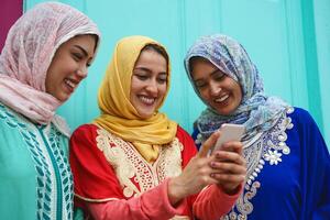 jovem muçulmano amigos assistindo em Móvel telefone ao ar livre - feliz árabe meninas viciado para Novo tecnologia Smartphone aplicativo para social meios de comunicação - juventude milenar pessoas e religião conceito foto