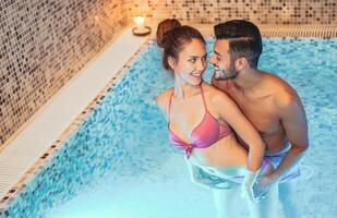 feliz casal tendo Diversão dentro natação piscina luxo spa recorrer hotel - romântico jovem pessoas fazendo relaxante bem estar tratamento juntos - amor relação e saúde estilo de vida conceito foto