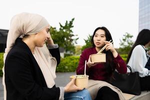 multirracial o negócio mulheres levando uma pausa para comendo uma refeição lado de fora a escritório foto