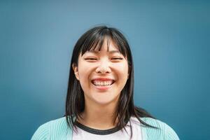 retrato do jovem ásia menina sorridente às Câmera - feliz chinês mulher tendo Diversão posando contra azul fundo - adolescente, na moda, milenar geração e juventude pessoas estilo de vida foto