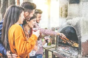 jovem pessoas tendo uma churrasco festa dentro a quintal em montanha - feliz amigos grelhar carne e bebendo vermelho vinho ao ar livre - amizade, estilo de vida e Comida conceito - foco em masculino mão certo foto