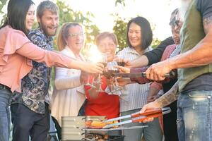 feliz família torcendo e brindar com vermelho vinho dentro churrasco festa - chefe de cozinha Senior homem grelhar carne e tendo com pais - final de semana Comida churrasco e reunião jovem e Mais velho pessoas estilo de vida conceito foto