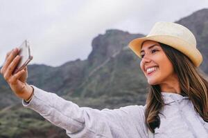 jovem lindo mulher dentro período de férias levando uma selfie com dela Móvel Smartphone Câmera com montanha dentro a fundo - telefone, social, vício e viagem conceito foto