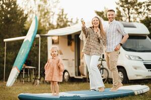 a família é em repouso Próximo para seus Móvel lar. pai, mãe e filha jogar em sup Pranchas com água pistolas perto a motorhome foto