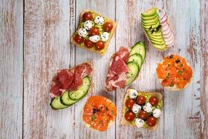 a sortimento do sanduíches com peixe, queijo, carne e legumes deitar em a de madeira mesa foto