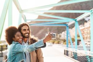 feliz sorridente casal levando selfie com Móvel Smartphone ao ar livre - jovem na moda pessoas tendo Diversão durante Férias - social pessoas tecnologia viciado e viagem tendência estilo de vida conceito foto