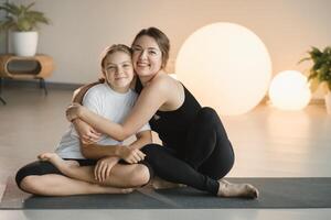 retrato do uma mãe e filha do uma adolescente dentro Esportes roupas abraçando, quem estão juntos dentro uma ginástica sala. a conceito do família Esportes foto