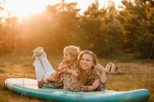 mãe e filha em uma sup borda dentro a floresta às pôr do sol foto