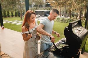 uma casado casal cozinheiros grelhado carne juntos em seus terraço foto