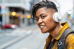 africano mulher ouvindo para música com sem fio fones de ouvido enquanto esperando para público transporte dentro a cidade rua foto