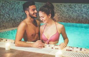 feliz casal em pé juntos dentro uma natação piscina spa Centro - romântico amantes tendo uma concurso momento em período de férias dentro recorrer bem estar hotel - relação, relaxamento e amor conceito foto