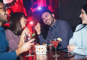 grupo do feliz amigos bebendo coquetéis dentro uma jazz coquetel Barra - milenar jovem pessoas tendo Diversão e rindo juntos dentro americano bar - amizade, vida noturna e juventude estilo de vida feriados foto