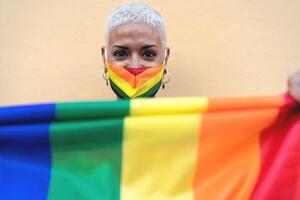 jovem mulher vestindo gay orgulho mascarar segurando arco Iris bandeira símbolo do lgbtq social movimento foto