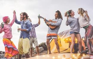 grupo amigos fazendo festa jogando guitarra e acampamento ao ar livre - feliz jovem pessoas tendo Diversão bebendo Cerveja e rindo dentro acampamento Vila - juventude cultura estilo de vida e período de férias viagem conceito foto