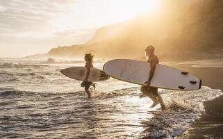 feliz em forma amigos surfar juntos em tropical de praia às pôr do sol Tempo - pessoas estilo de vida e extremo esporte conceito foto