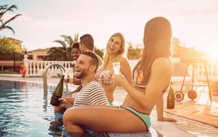 grupo do feliz amigos fazer uma piscina festa às pôr do sol - jovem pessoas rindo e tendo Diversão bebendo champanhe dentro período de férias - amizade, feriados, juventude estilo de vida conceito foto