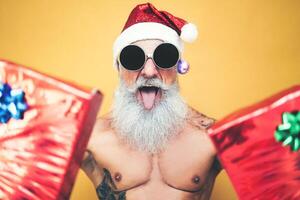 tatuado em forma santa claus fazendo louco e dando Natal presentes - na moda barba hipster Senior vestindo natal roupas e segurando apresenta - x-mas celebração e feriados conceito foto