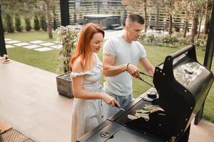 uma casado casal cozinheiros grelhado carne juntos em seus terraço foto
