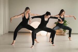 uma grupo do meninas dentro Preto fazendo ioga poses dentro de casa. mulheres estão acionado dentro ginástica foto