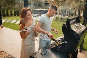 uma casado casal cozinheiros grelhado carne juntos em seus terraço foto