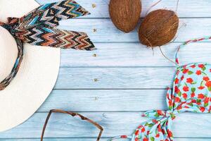 topo Visão do uma Palha branco chapéu com copos, uma roupa de banho e uma coco deitado em uma azul de madeira background.summer período de férias conceito foto