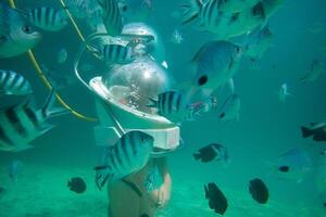 uma menina dentro uma ampla embaixo da agua capacete parece às peixe embaixo da agua dentro uma coral recife em a ilha do Maurícia foto