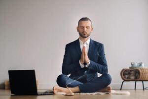 uma homem dentro uma formal terno medita enquanto sentado dentro uma ginástica quarto com uma computador portátil foto