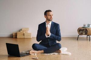 uma homem dentro uma formal terno medita enquanto sentado dentro uma ginástica quarto com uma computador portátil foto