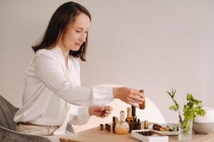 a aromaterapeuta menina é sentado dentro dela escritório. lá estão essencial óleos em a mesa foto