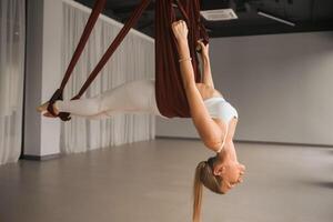 uma menina dentro branco roupa de esporte faz ioga em uma suspensão maca dentro a ginástica quarto foto