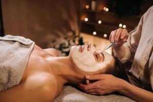 uma cosmetologista faz uma mascarar para uma mulher face para rejuvenescer a pele. cosmetologia foto
