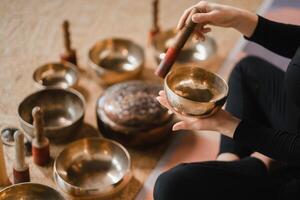 fechar-se do uma mulher mãos sentado dentro uma lótus posição usando uma cantando tigela dentro de casa. relaxamento e meditação. som terapia, alternativo remédio. tibetano taças foto