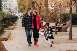 uma pequeno menina com dela pais corre para a outono cidade.a à moda família do três passeios através a outono cidade foto