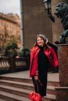 uma lindo à moda mulher vestido dentro a elegante vermelho casaco com uma à moda vermelho Bolsa dentro a outono cidade foto