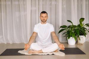 uma homem dentro branco roupa de esporte é fazendo ioga com uma ginástica sala. a conceito do uma saudável estilo de vida foto