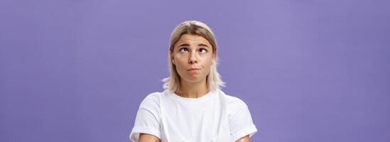 mente indo louco. retrato do engraçado cansado atraente jovem mulher com justo cabelo e bronzeada pele apertando os olhos rolando olhos a parte, de lado e olhando acima enganar por aí sobre roxa fundo a partir de tédio foto