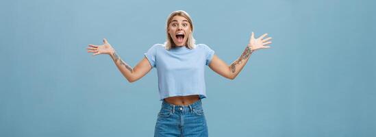 menina sobrecarregado com positivo emoções e felicidade ser surpreso alegria e gritando a partir de alegria espalhando Palmeiras a parte, de lado abertura boca a partir de espanto em pé Deleitado sobre azul parede foto