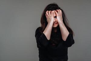 uma maltratado mulher dentro Preto roupas em a isolado cinzento fundo. violência contra mulheres foto