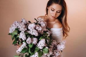 lindo menina com lilás flores dentro dela mãos. uma menina com lilás flores dentro a Primavera às lar. uma menina com grandes cabelo e lilás dentro dela mãos foto